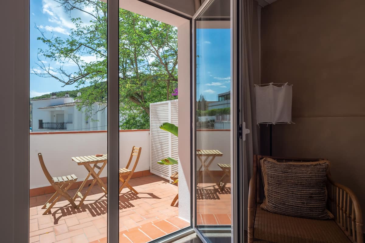 Un balcón con muebles de madera, una silla de mimbre y vistas a edificios y árboles.