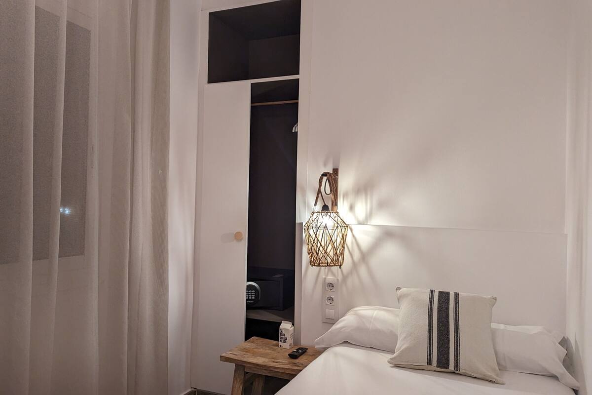 Una habitación de hotel con cama, mesita de noche, lámpara y armario.