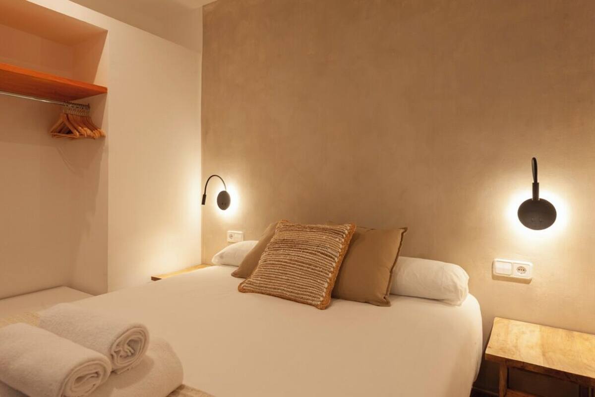 Habitación de hotel con una cama, dos lámparas de pared, una mesita de noche de madera y un perchero para toallas.