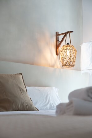Una cama bien hecha con sábanas blancas, un almohábil beige y una lámpara fijada a la pared.