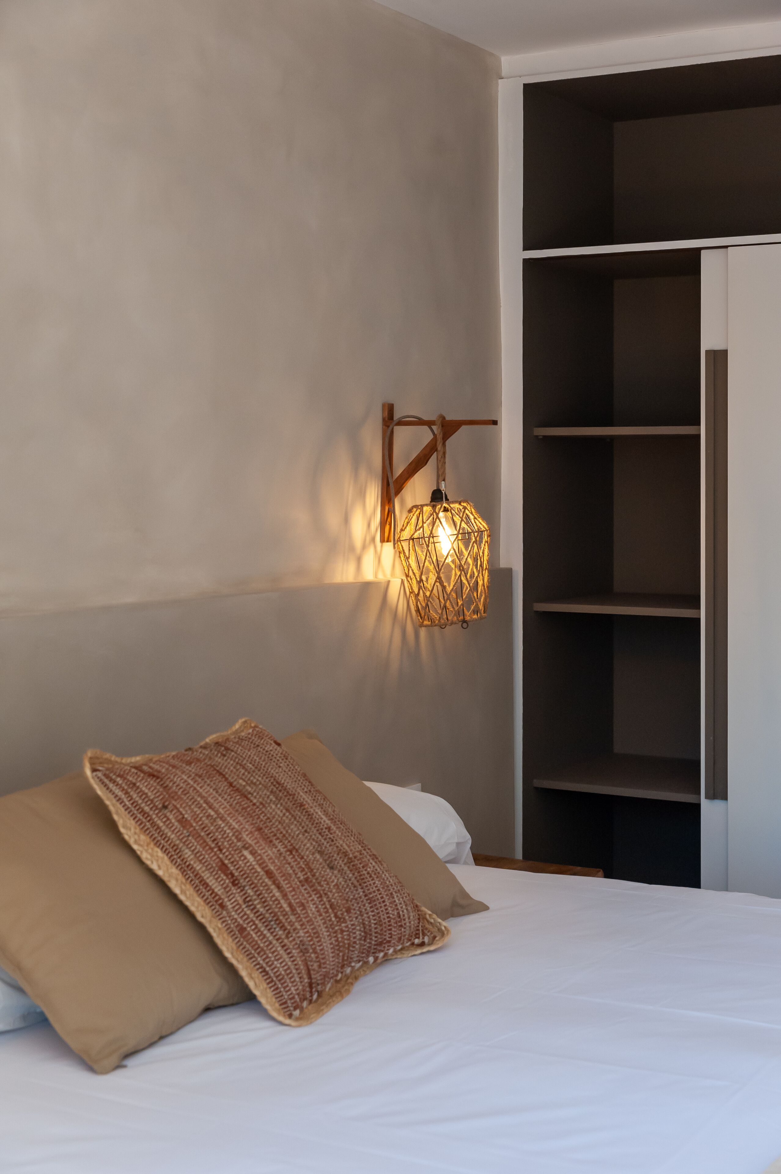 A bedroom with a bed, a woven throw blanket, a wall-mounted lamp, and a built-in wardrobe.