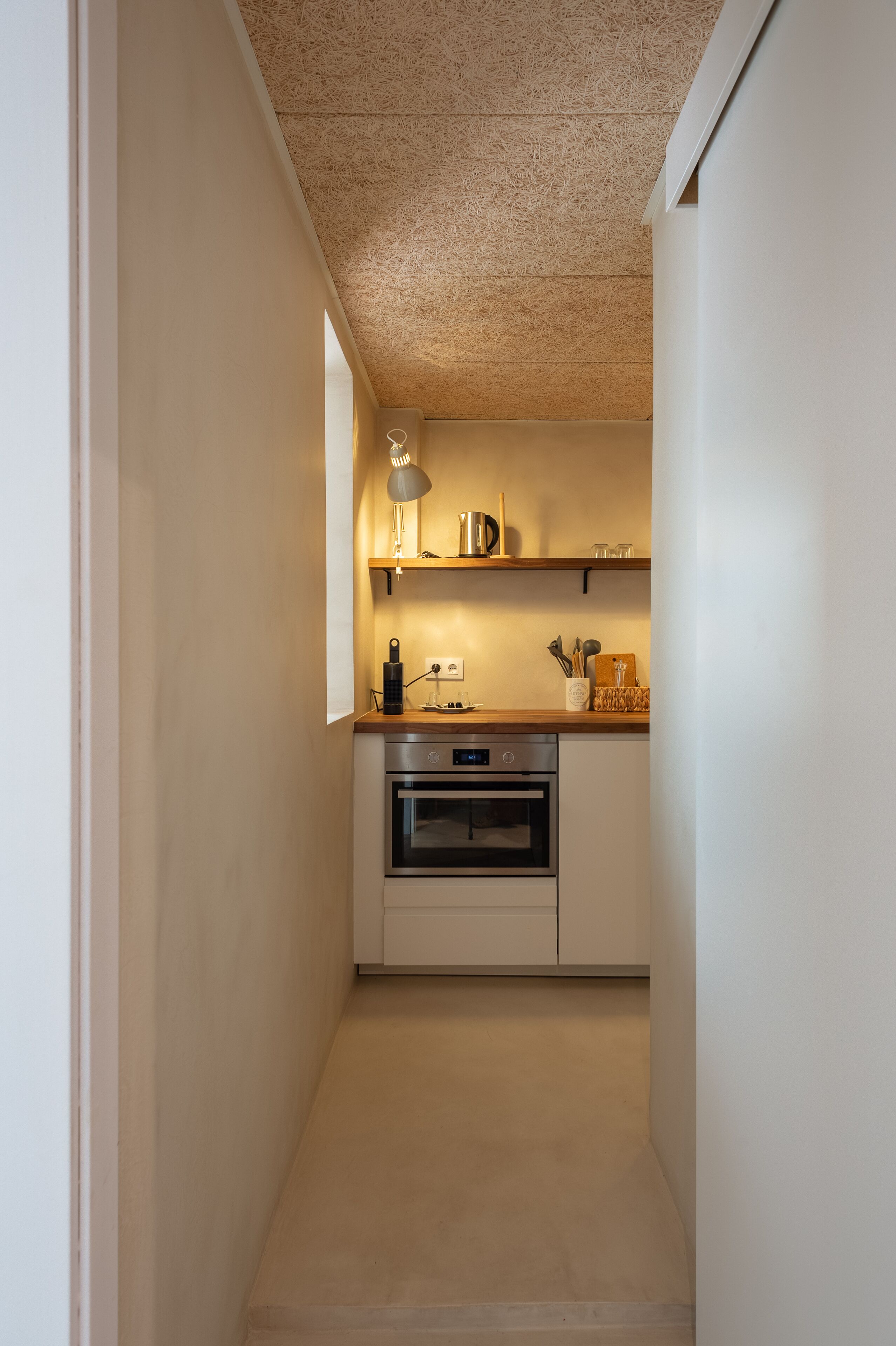 Una cocina estrecha con armarios blancos, una encimera de madera y una lámpara colgante.