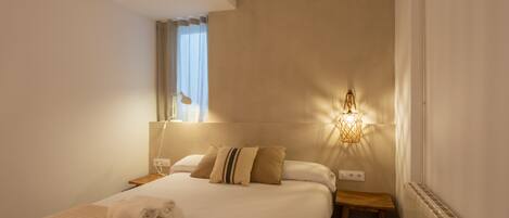A hotel room with a large bed, a bedside table, a nightstand, a lamp, and a radiator.