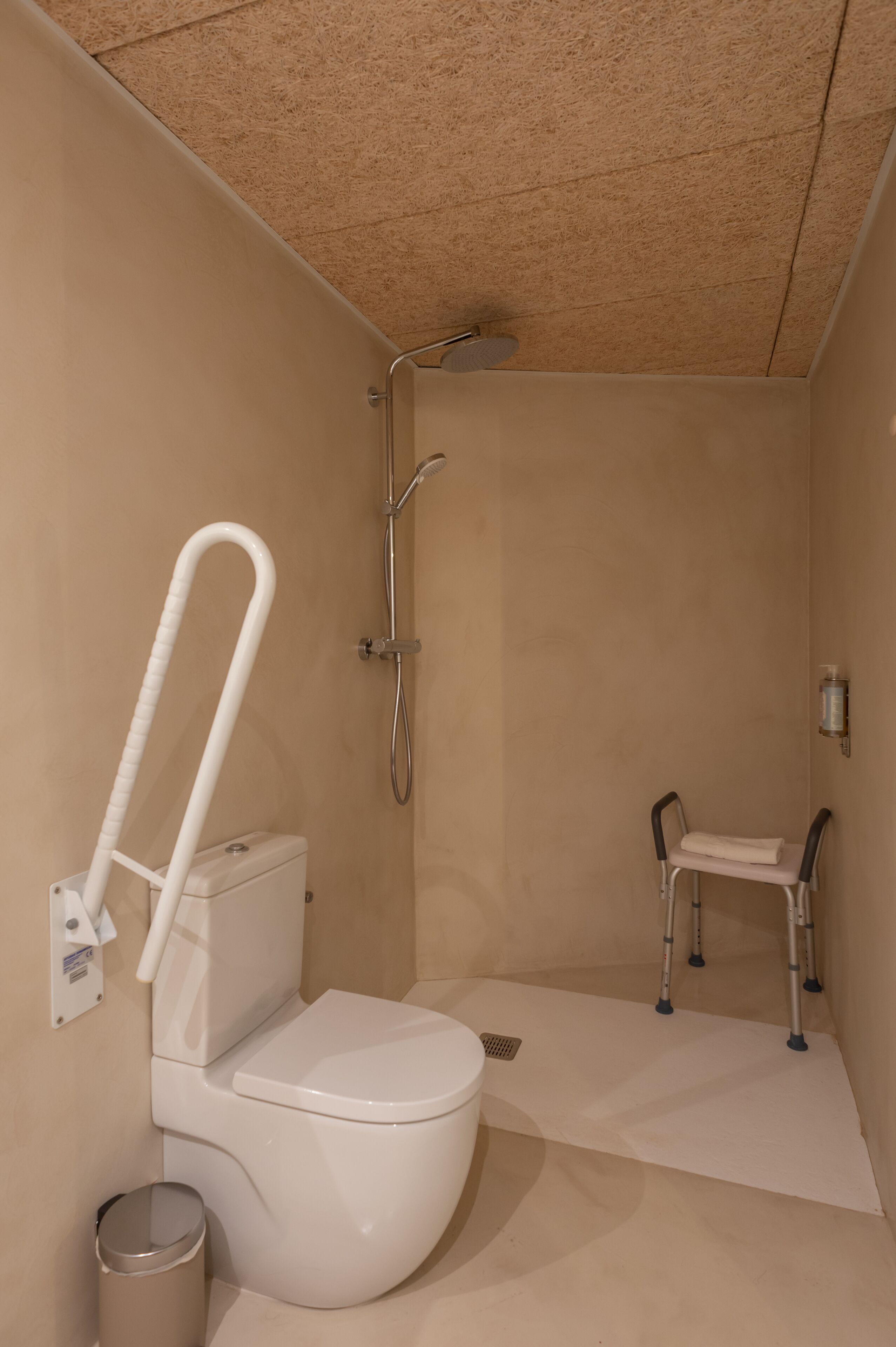 Un baño pequeño individual con inodoro, ducha y un banco accesible en silla de ruedas.