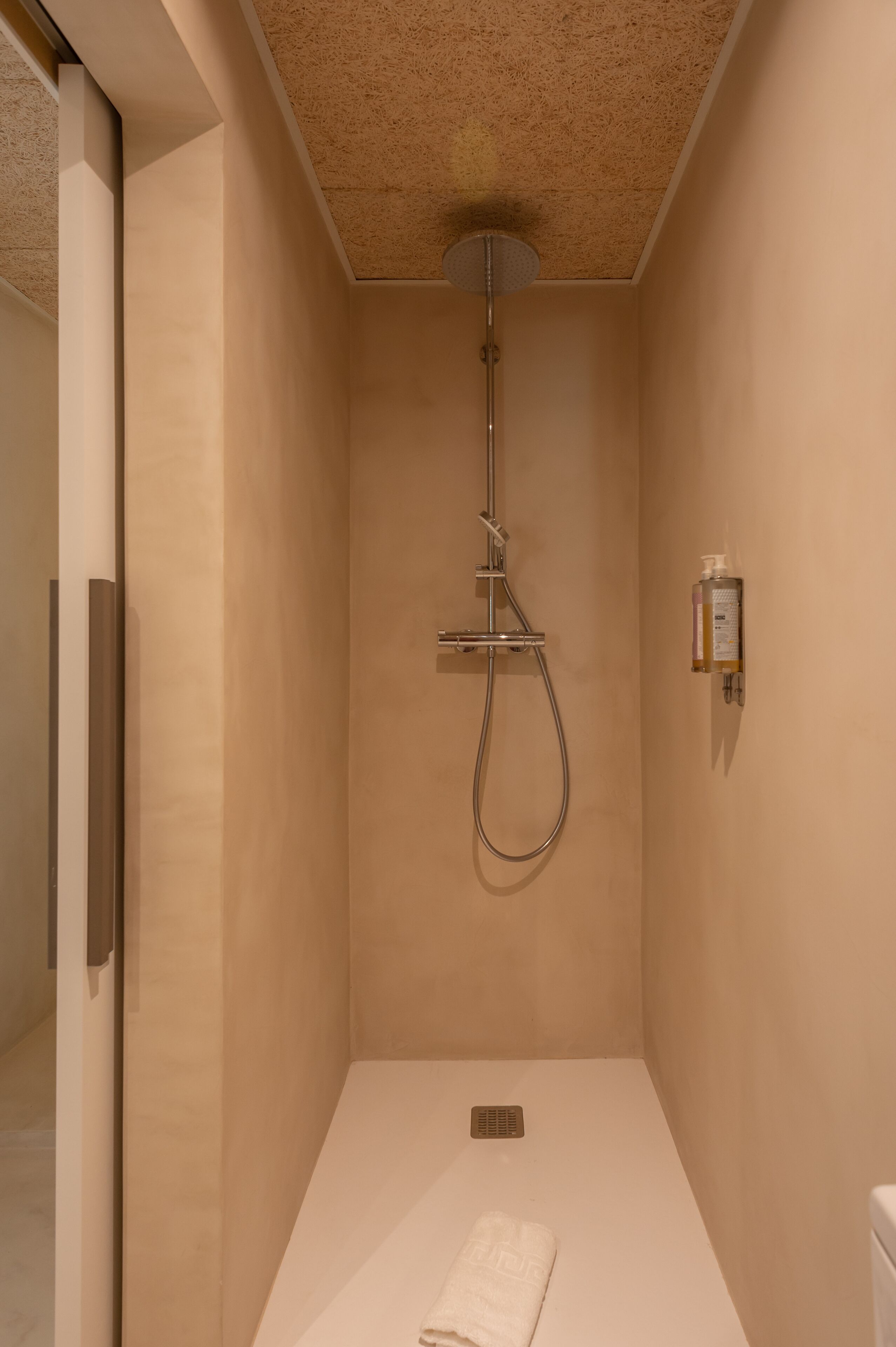 A modern shower room with a handheld showerhead, a wall-mounted soap dispenser, and a towel on the floor.