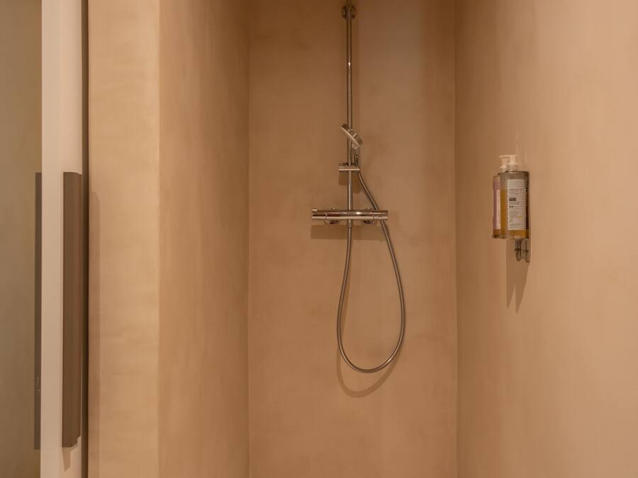 A modern shower room with a handheld showerhead, a wall-mounted soap dispenser, and a towel on the floor.