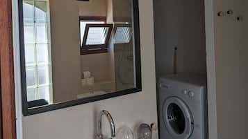 A bathroom with a white sink, a mirror, a black pendant light, a window, and a washing machine.