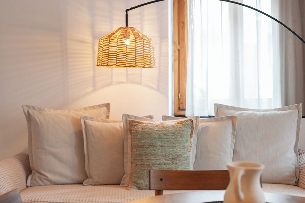 Un coin salon confortable avec un luminaire suspendu en fibres tressées, des coussins moelleux et une chaise en bois.