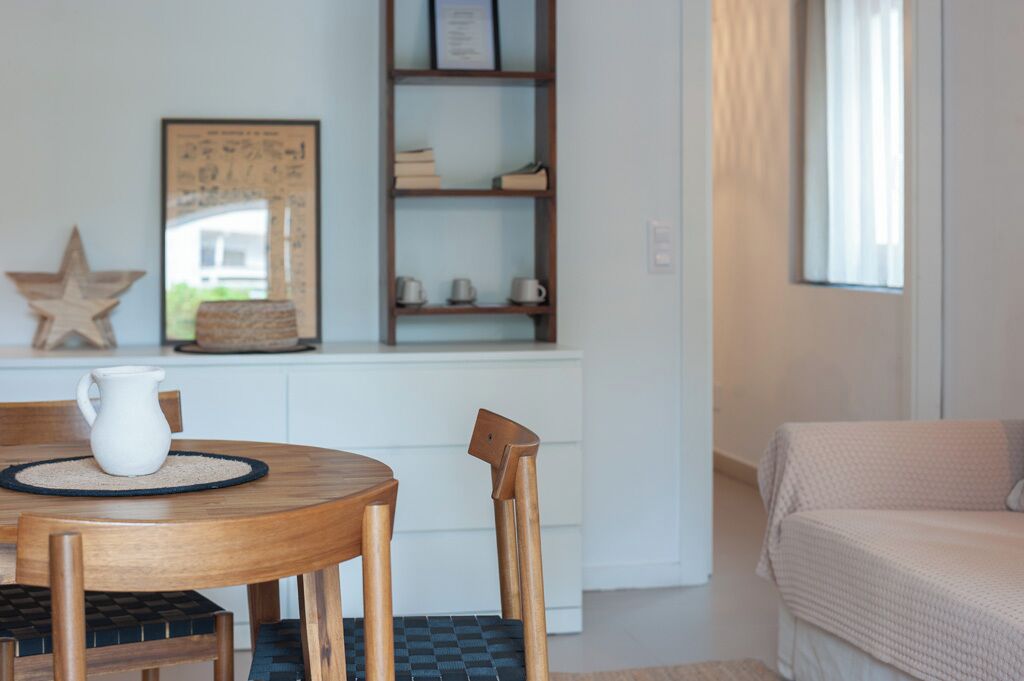 A cozy room with a wooden table and chairs, a bookshelf, a bed, and a window with curtains.