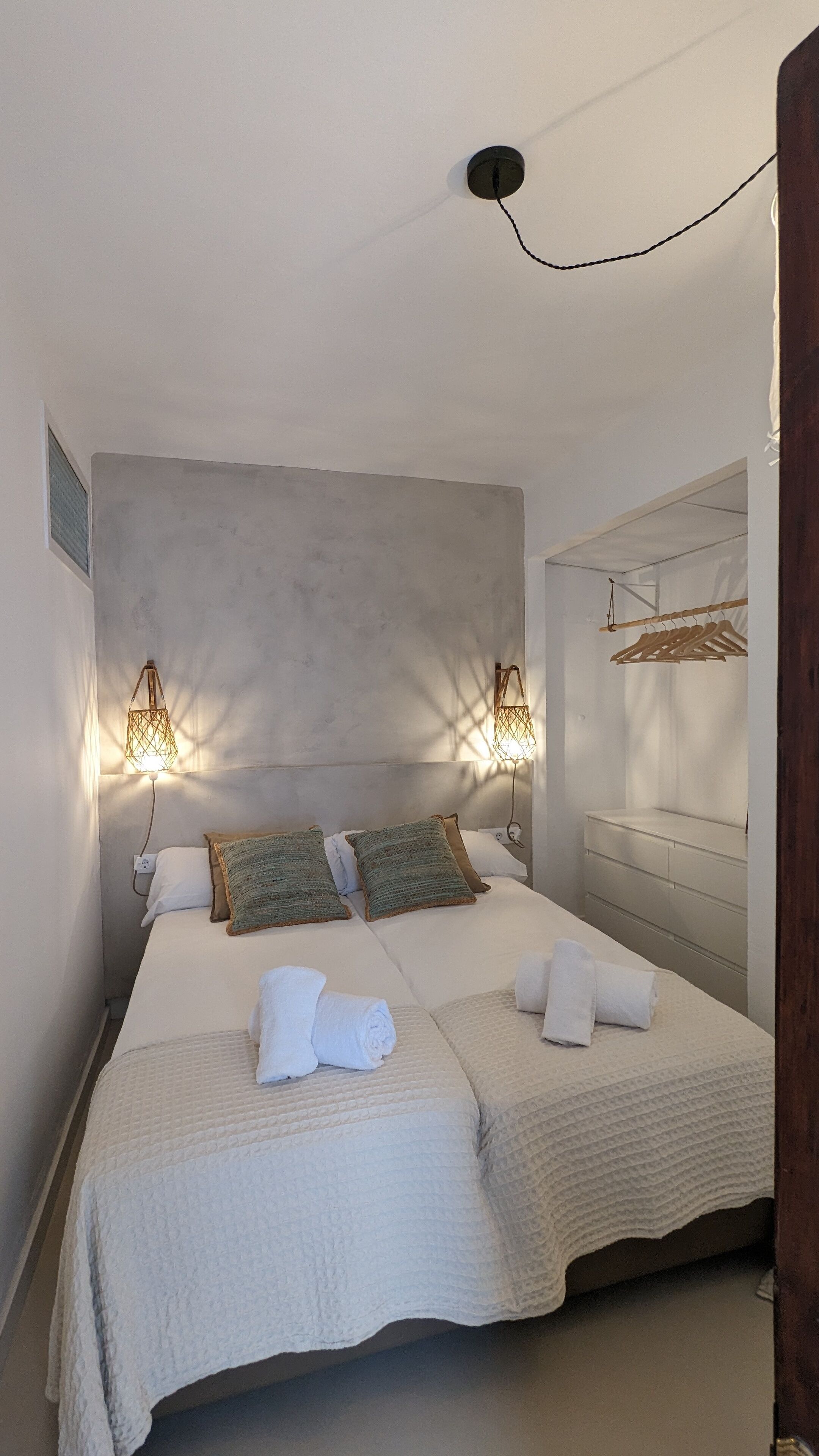 A double bed with two pillows, a bedside table, and a hanging wooden rack.