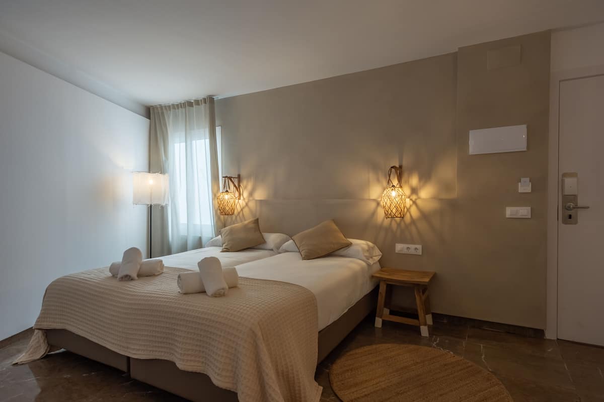 Habitación de hotel con una cama grande, dos lámparas de noche, un taburete de madera y un tapete redondo.