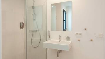 Un baño moderno con ducha de vidrio, un lavamanos blanco y un espejo sobre él.