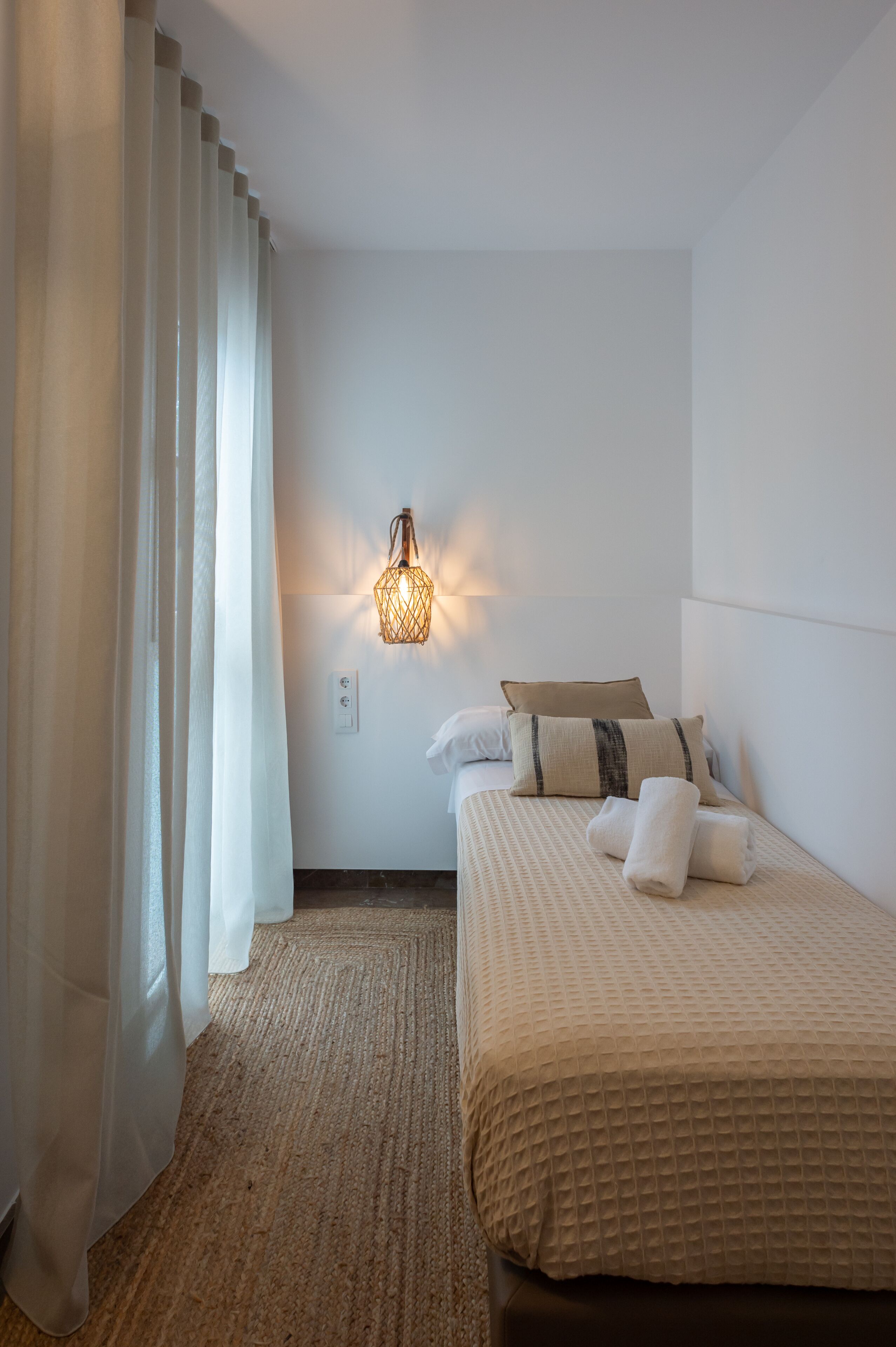 Una camera d'albergo con un letto, un lampadario a parete e una finestra con tende.