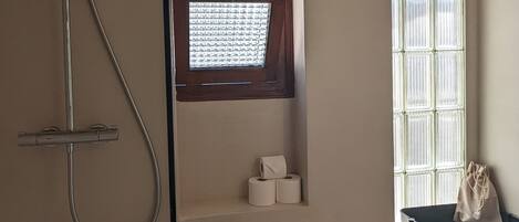 A bathroom with a shower, toilet, and a window with blinds.