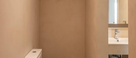A modern bathroom with a white toilet, a small mirror, and a shelf with toiletries.