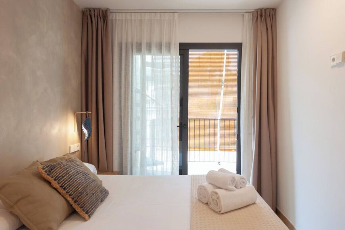 Una habitación de hotel con cama, ventana con cortinas y vistas al exterior.