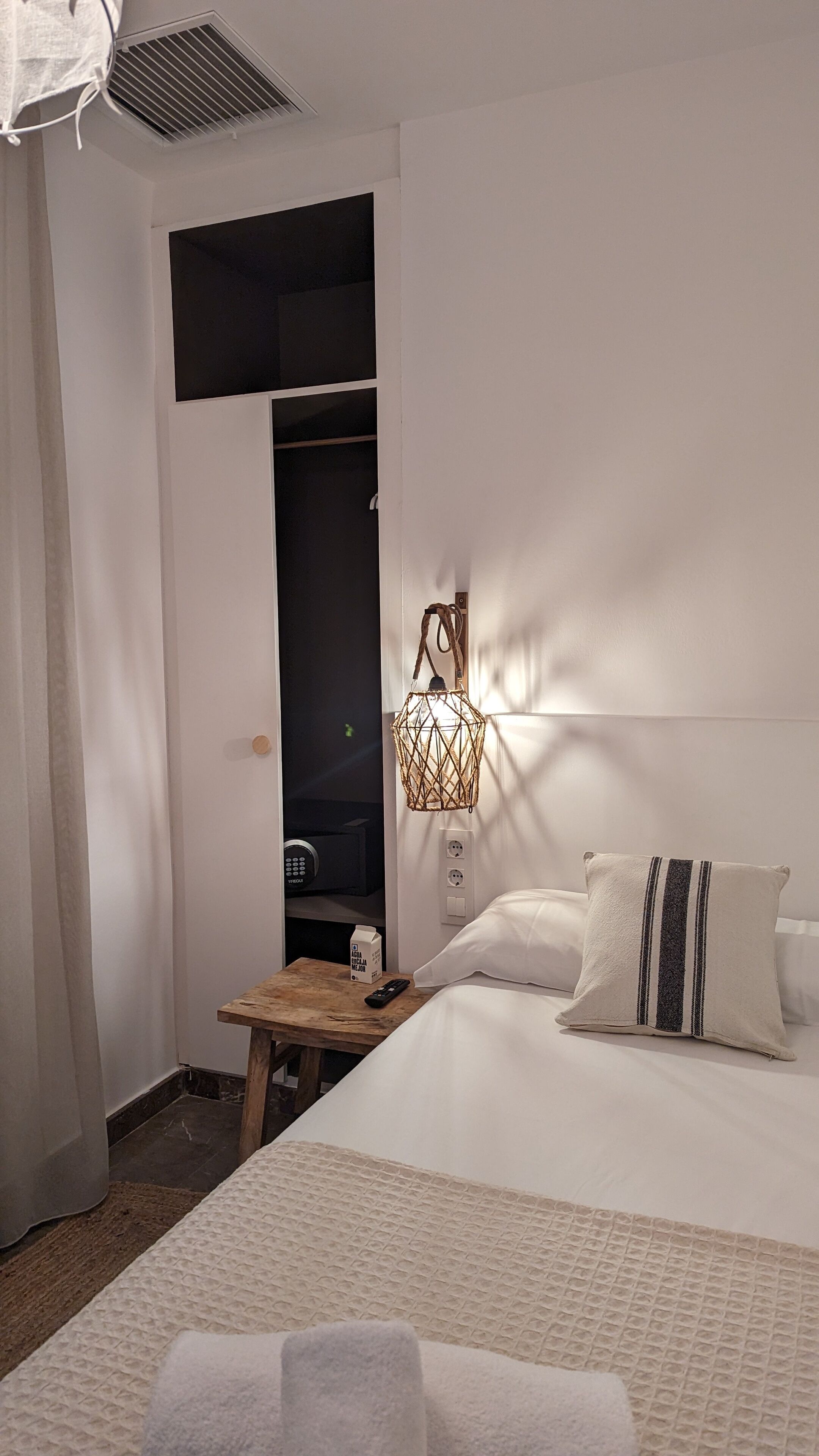A hotel room with a bed, bedside table, lamp, and a wardrobe.