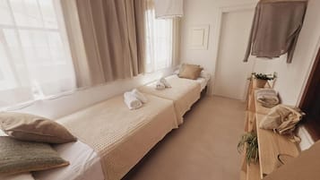 A hotel room with two single beds, a hanging light fixture, a small table with a plant, and a coat rack.