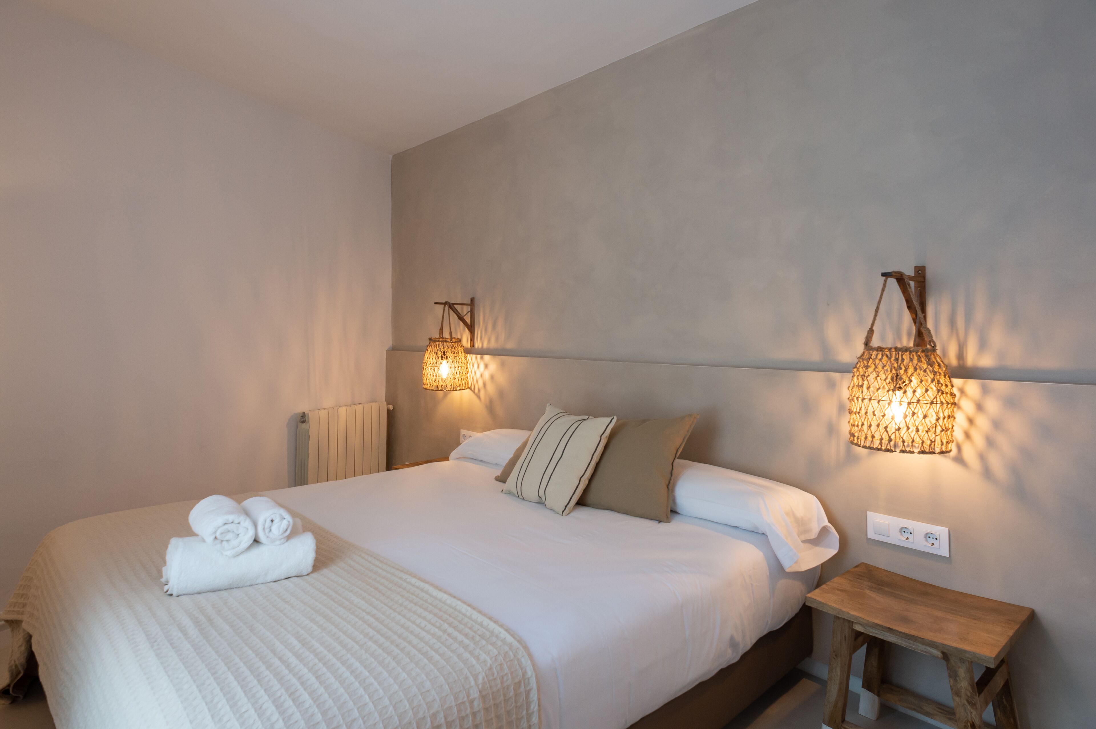 A neatly made bed with rolled towels, a bedside table, and wall-mounted lamps.