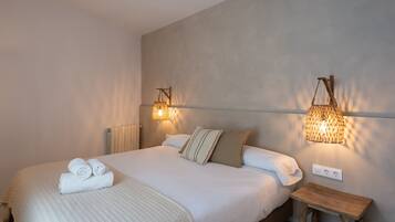 A neatly made bed with rolled towels, a bedside table, and wall-mounted lamps.