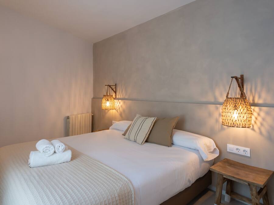 A neatly made bed with rolled towels, a bedside table, and wall-mounted lamps.