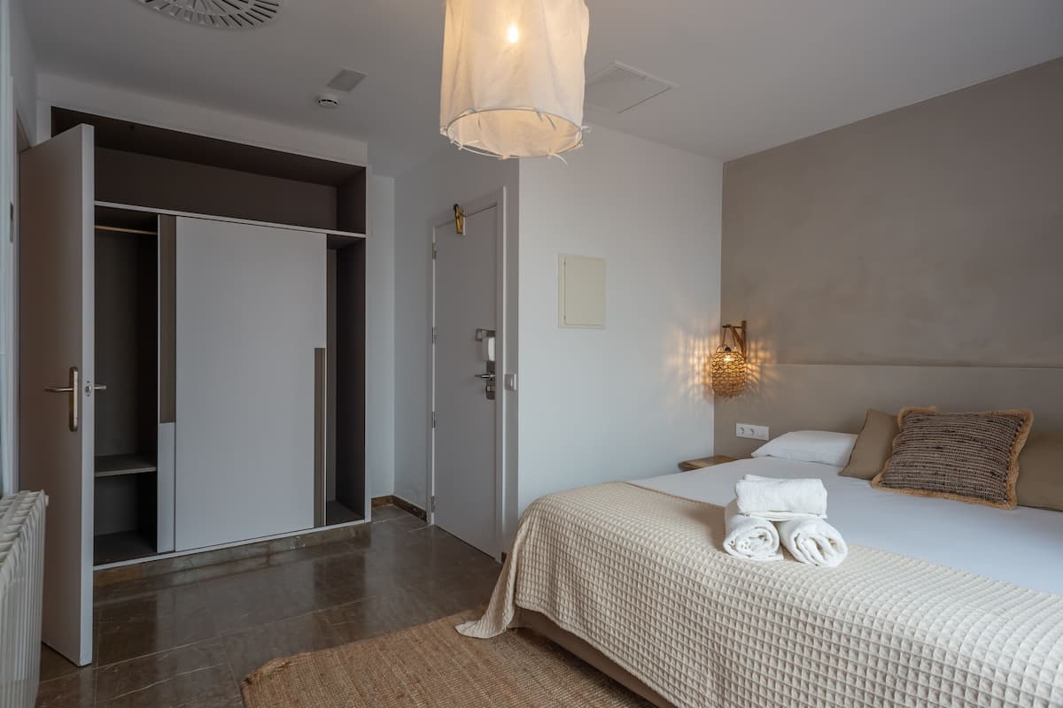 Una habitación de hotel con cama, armario, luz empotrada en la pared y radiador.