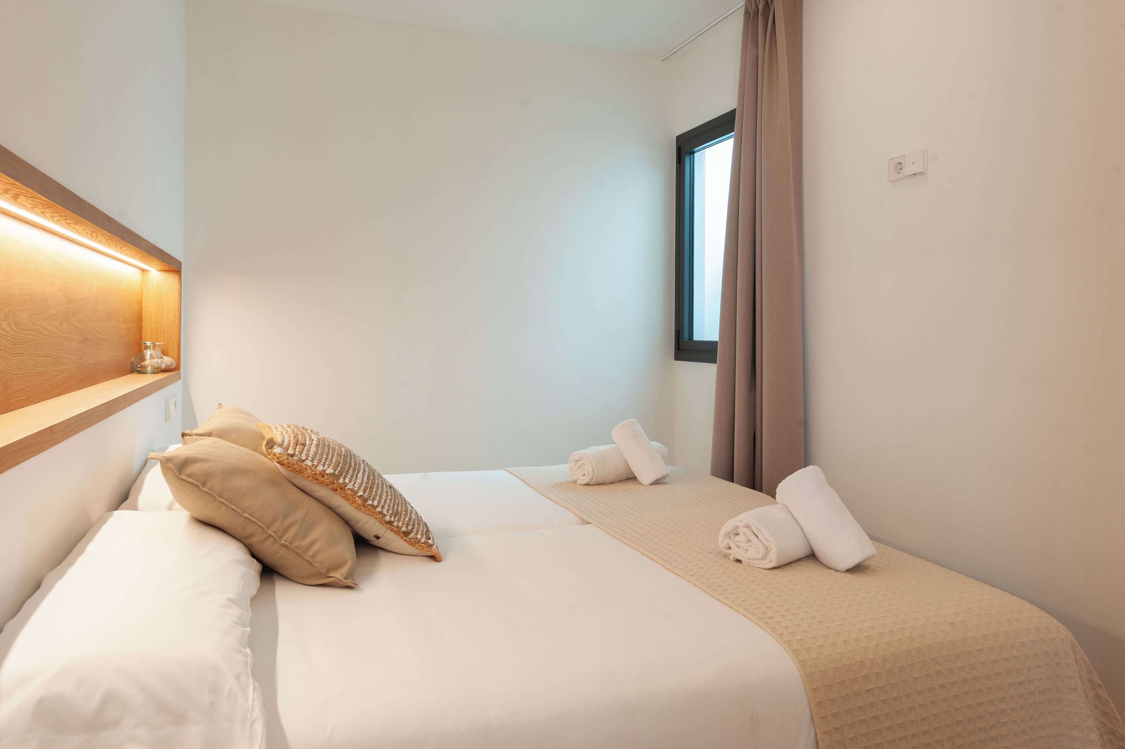 A hotel room with a bed, two pillows, a window, and a wall-mounted light.