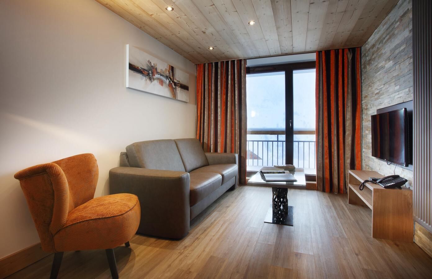 Ein modernes Wohnzimmer mit Sofa, Sessel und einem an der Wand befestigten Flachbildfernseher.