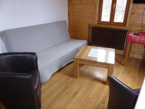 A cozy room with a grey sofa, a wooden coffee table, and two black chairs.