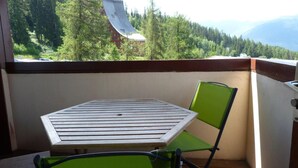 Een balkon met een tafel en stoel, met uitzicht op een bebost gebied en bergen in de verte.