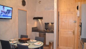 A compact kitchen with a dining area, a television displaying news, and a wooden door. - 10m from ski slopes, 13rd floor, view mountain, tv, 25m², Les Menuires (Les Menuires)