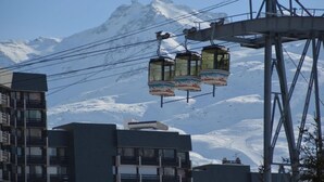 A cable car system with three gondolas, a mountain backdrop, and modern buildings in the foreground. - 10m from ski slopes, 13rd floor, view mountain, tv, 25m², Les Menuires (Les Menuires)