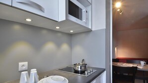 A compact kitchenette with a microwave, stove, and sink. There are white plates and cups on the counter. - Ski-in/ski-out & foot of the slopes, 2nd floor, balcony, tv, 28m², La Plagne (La Plagne)