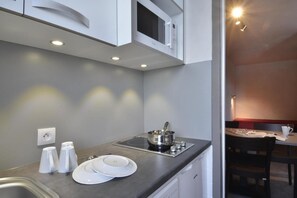 Una kitchenette compacta con microondas, estufa y pileta. Hay platos y tazas blancas en la encimera.