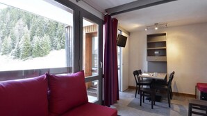 A room with a red sofa, a dining table with chairs, a TV mounted on the wall, and a window with curtains. - Ski-in/ski-out & foot of the slopes, 2nd floor, balcony, tv, 28m², La Plagne (La Plagne)