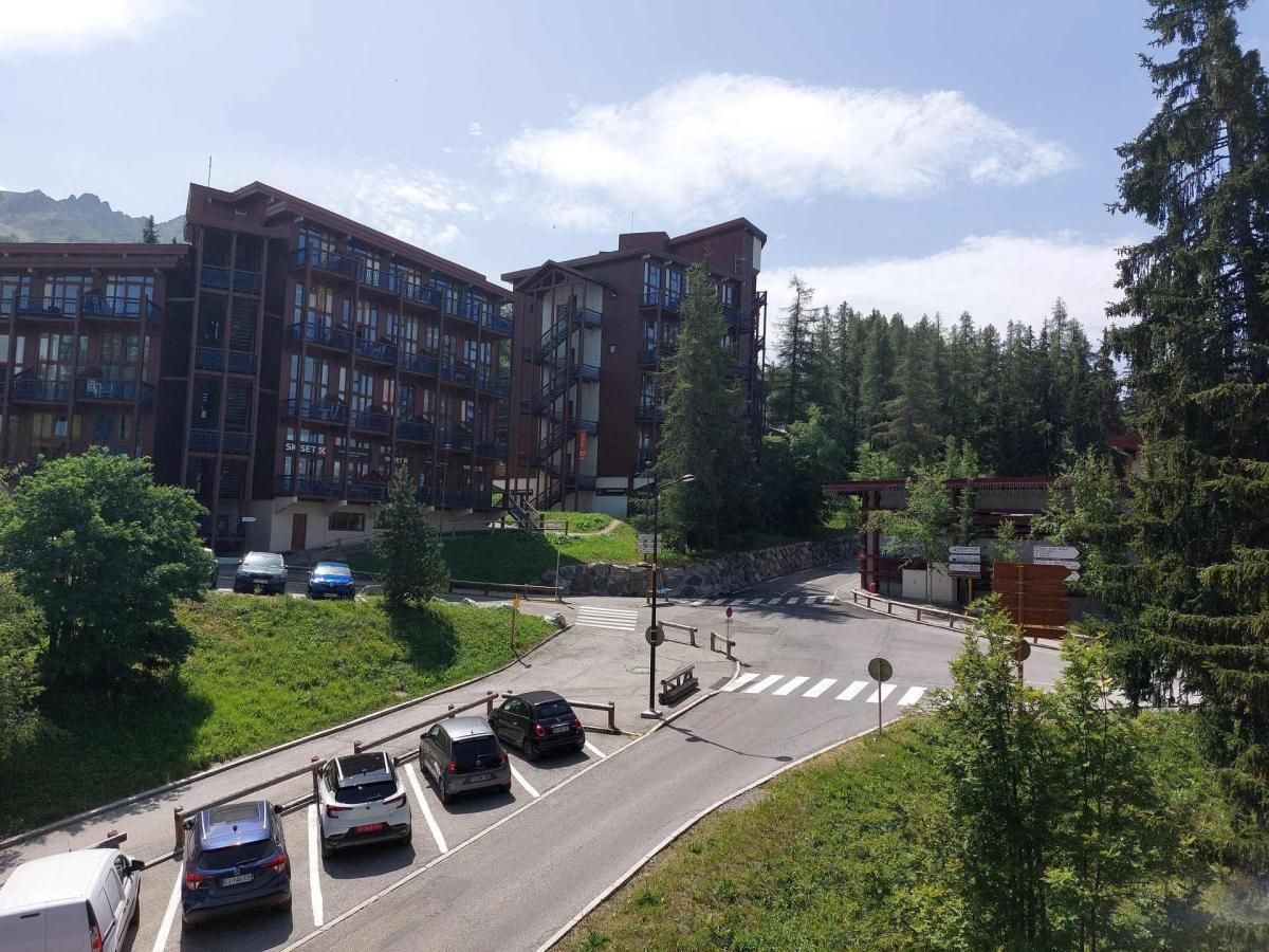 A multi-story building with balconies, a parking area with cars, and a crosswalk.