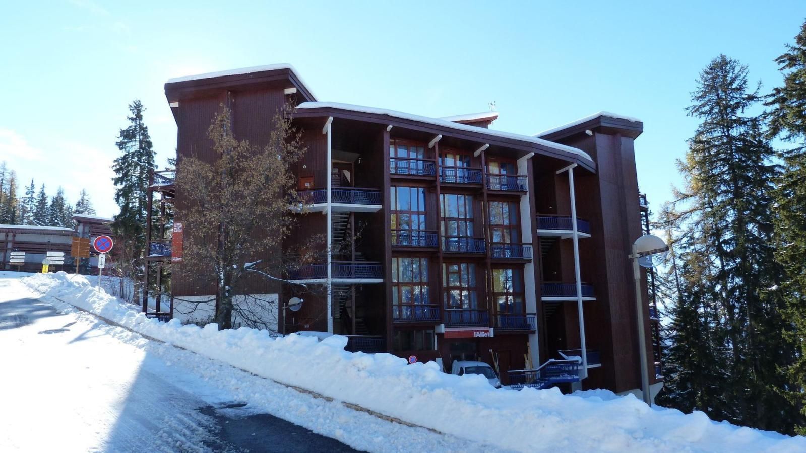 A multi-story building with balconies, a snow-covered ground, and a clear sky.