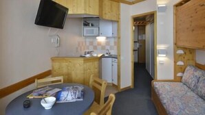 Ett kompakt rum med ett matbord, stolar, en soffa, en tv som är monterad på väggen och ett litet kök med mikrovågsugn.