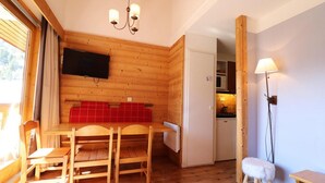 Un interior de madera con una mesa de comedor, sillas, un televisor montado en la pared, una zona de cocina y una lámpara.