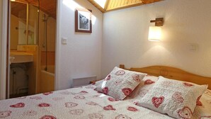 Un dormitorio con cama, almohadas, mesita de noche, lámpara de pared, un cuadro enmarcado y techo de madera.