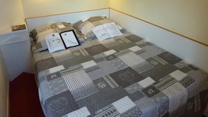 Ein ordentlich gemachtes Bett mit einem Patchwork-Quilt, zwei Nachttischlampen und einem gerahmten Bild an der Wand.