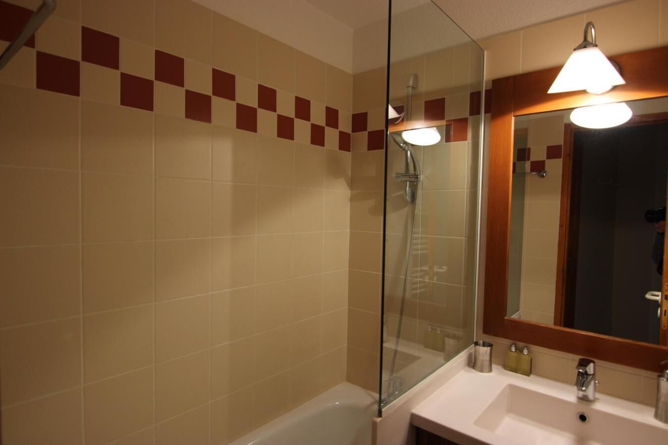 Une salle de bain avec une douche à parois de verre, un lavabo avec un miroir et un mur carrelé à motifs à carreaux.