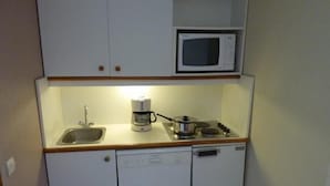 Eine kleine Küchenzeile mit Spüle, Kaffeemaschine, Mikrowelle und Herd.