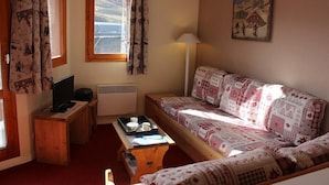 Ein gemütliches Zimmer mit einer Holzsofa, einem kleinen Tisch mit Tablett, einem Fernseher und einem Fenster mit Vorhängen.