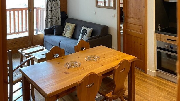 A cozy cabin interior with a wooden dining table, chairs, a sofa, and a kitchenette. - 150m from ski slopes, 2nd floor, balcony, tv, ski locker, 45m², Valloire (Valloire)