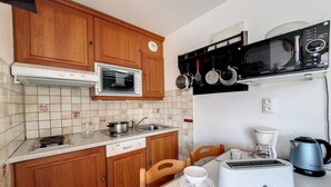 A compact kitchen with wooden cabinets, a built-in oven, a microwave, a toaster, and a coffee maker. - 2nd floor, tv, ski locker, 26m², Les Menuires (Les Menuires)