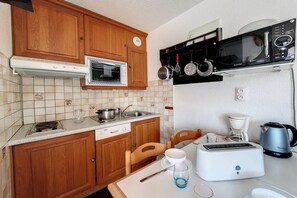 Une cuisine compacte dotée de meubles en bois, d’un four encastré, d’un four à micro-ondes, d’un grille-pain et d’une machine à café.