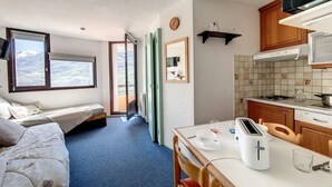 A compact room with a bed, a dining table with a toaster, a kitchen area with a microwave, and a view of mountains through the windows. - 2nd floor, tv, ski locker, 26m², Les Menuires (Les Menuires)