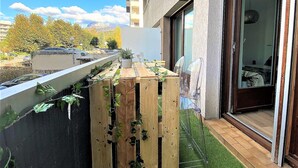 Ein Balkon mit Holzlatten, einem kleinen Tisch und einem Blumentopf sowie eine klare Glasdoor, die zu einem Zimmer führt.