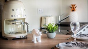 Eine Küche mit Kaffeemaschine, einer kleinen Topfpflanze, einer dekorativen Elefantenfigur, einem Weinglas und einem Teller mit schwarz-weißem Muster.